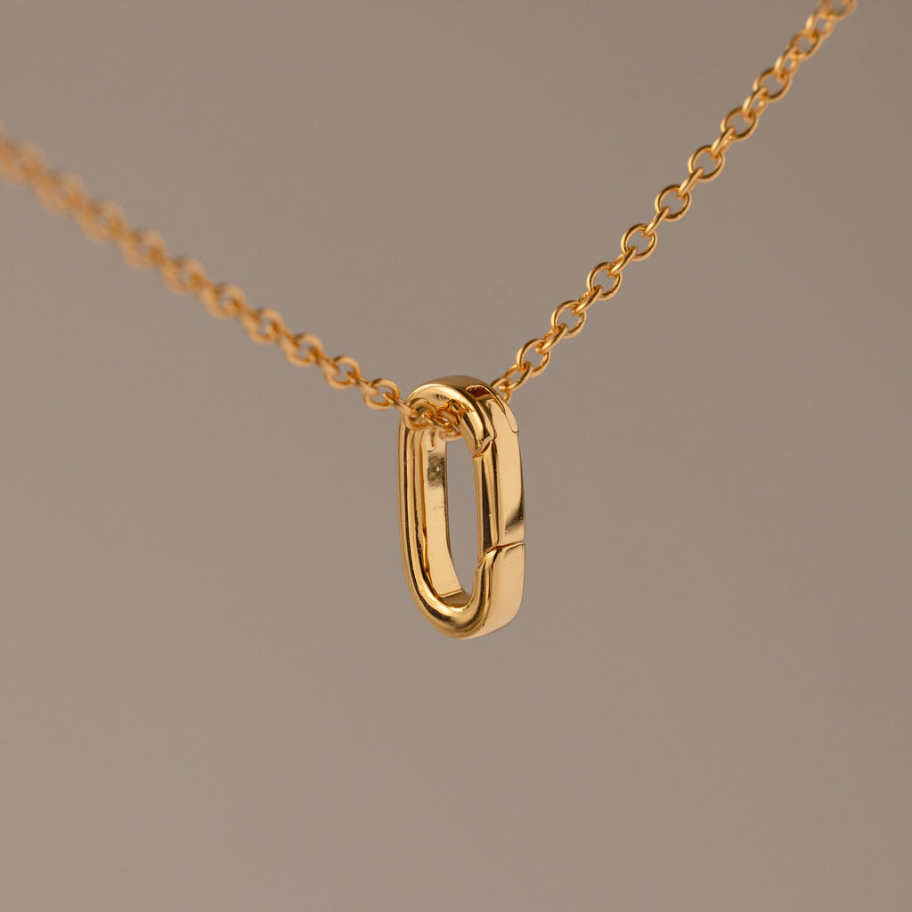 Multipurpose Charm Hoop Clasp Set in 18K Gold features a gold chain necklace with an oval pendant and a versatile charm hoop clasp, ideal for bracelet stacking, shown against a plain beige background.