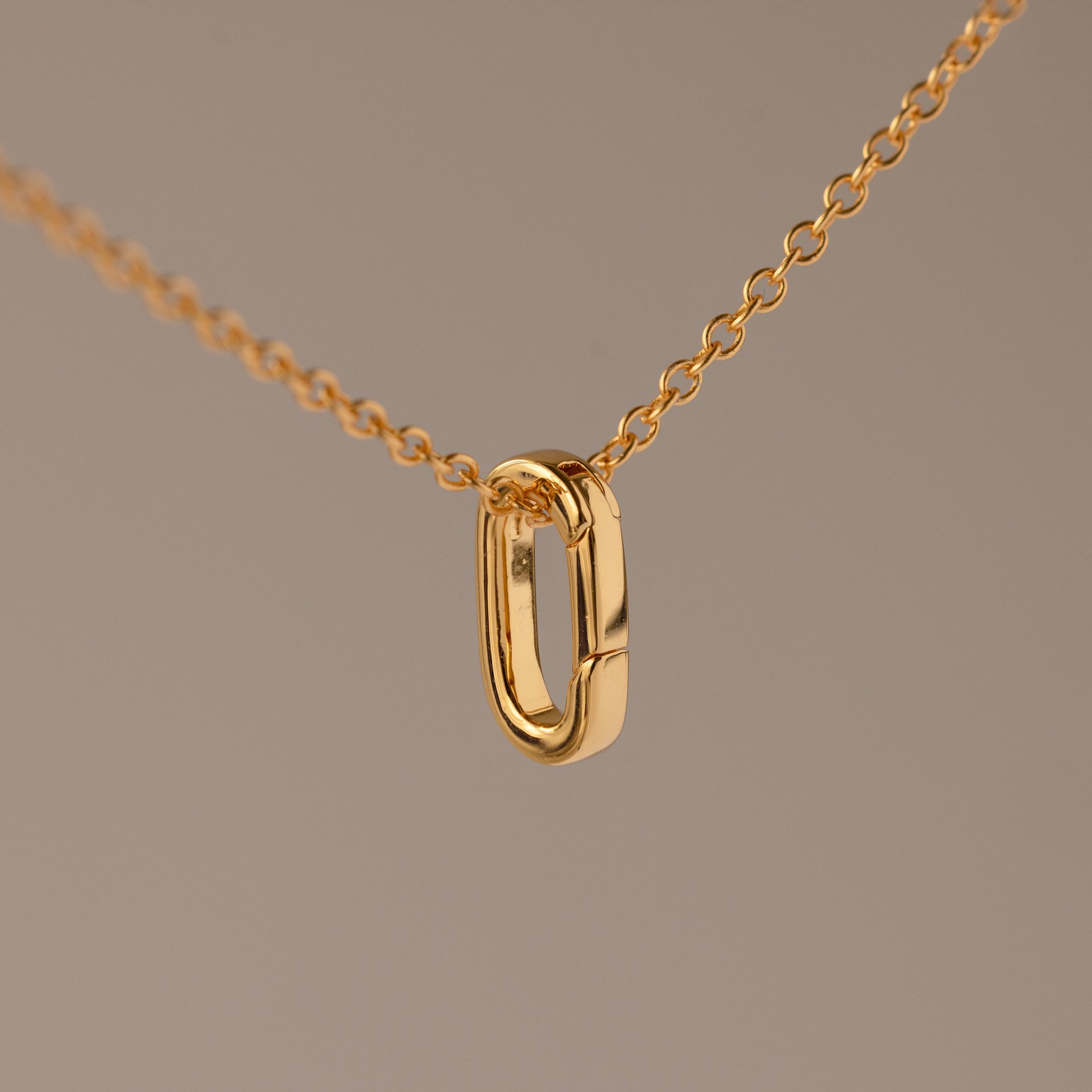 Multipurpose Charm Hoop Clasp Set in 18K Gold features a gold chain necklace with an oval pendant and a versatile charm hoop clasp, ideal for bracelet stacking, shown against a plain beige background.