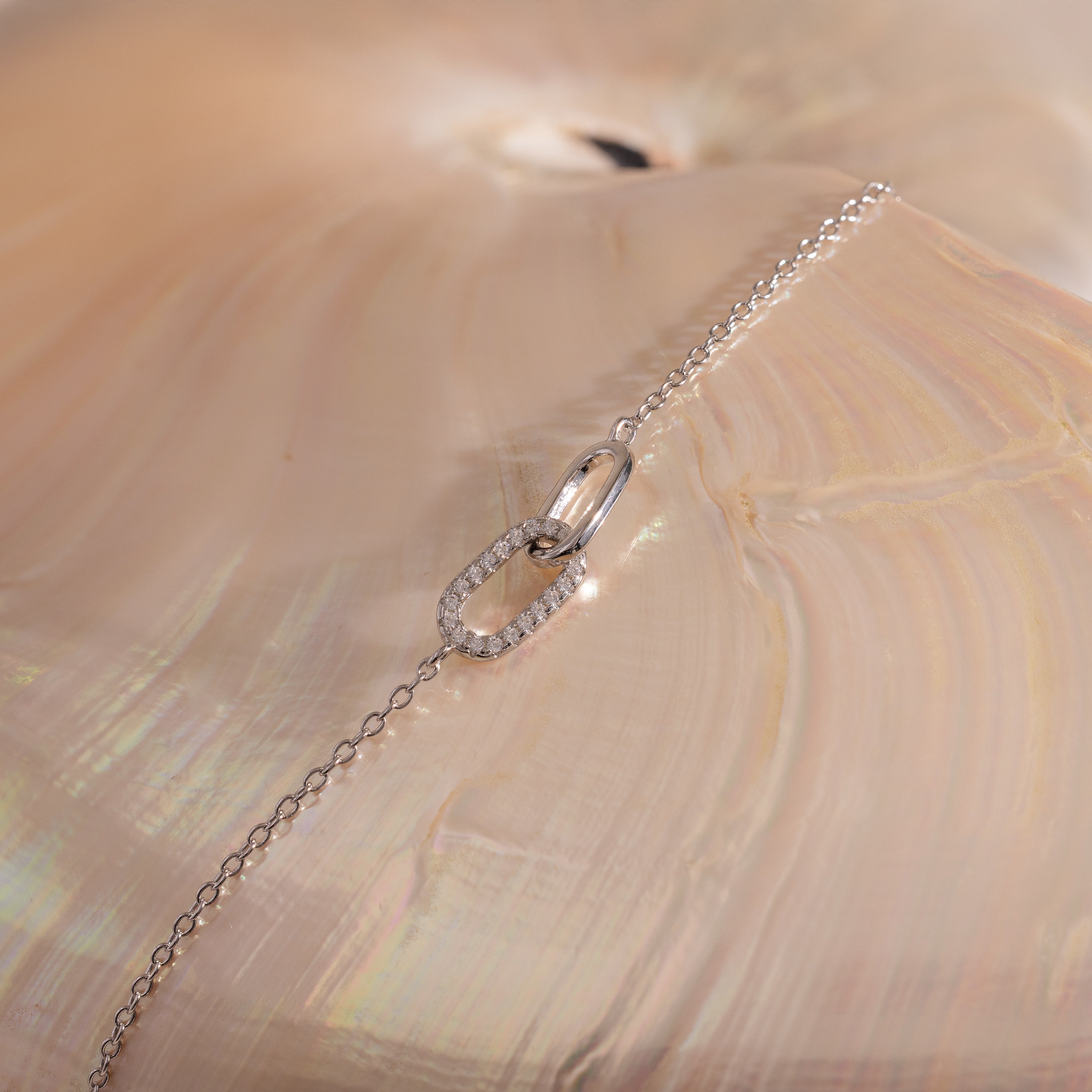 The Pave Linked Pendant Bracelet in Sterling Silver features interlocking links and a diamond-studded oval charm, displayed on a shiny, iridescent seashell background.