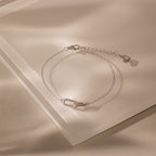 Close-up of a dainty silver chain bracelet featuring two interlocking links charms, one circle and one oval link.