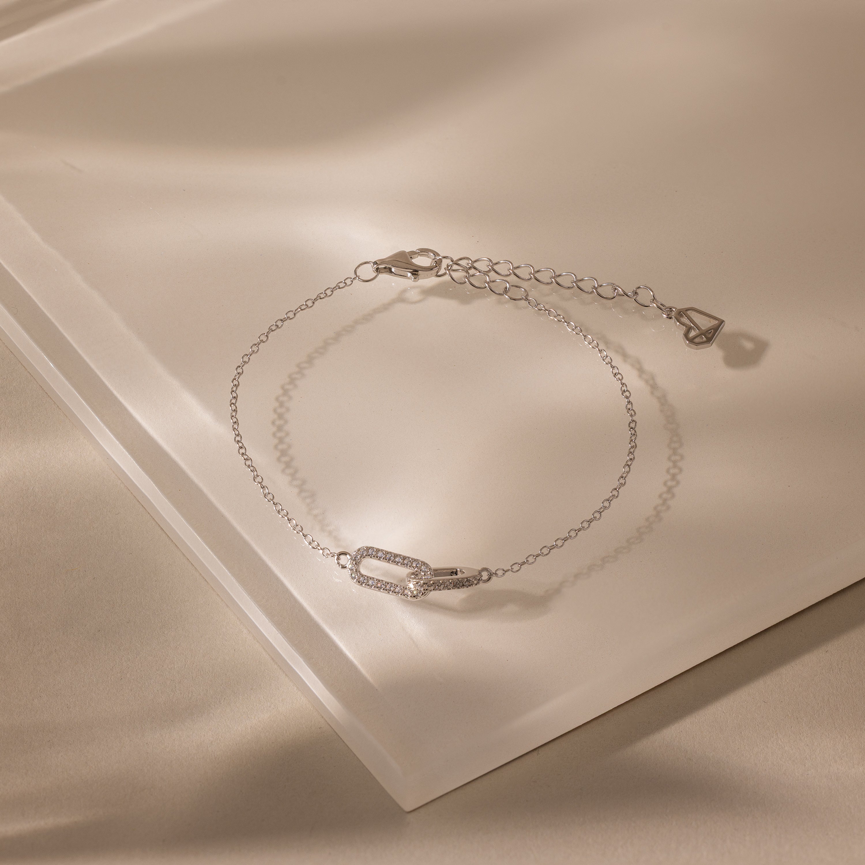 Close-up of a dainty silver chain bracelet featuring two interlocking links charms, one circle and one oval link.