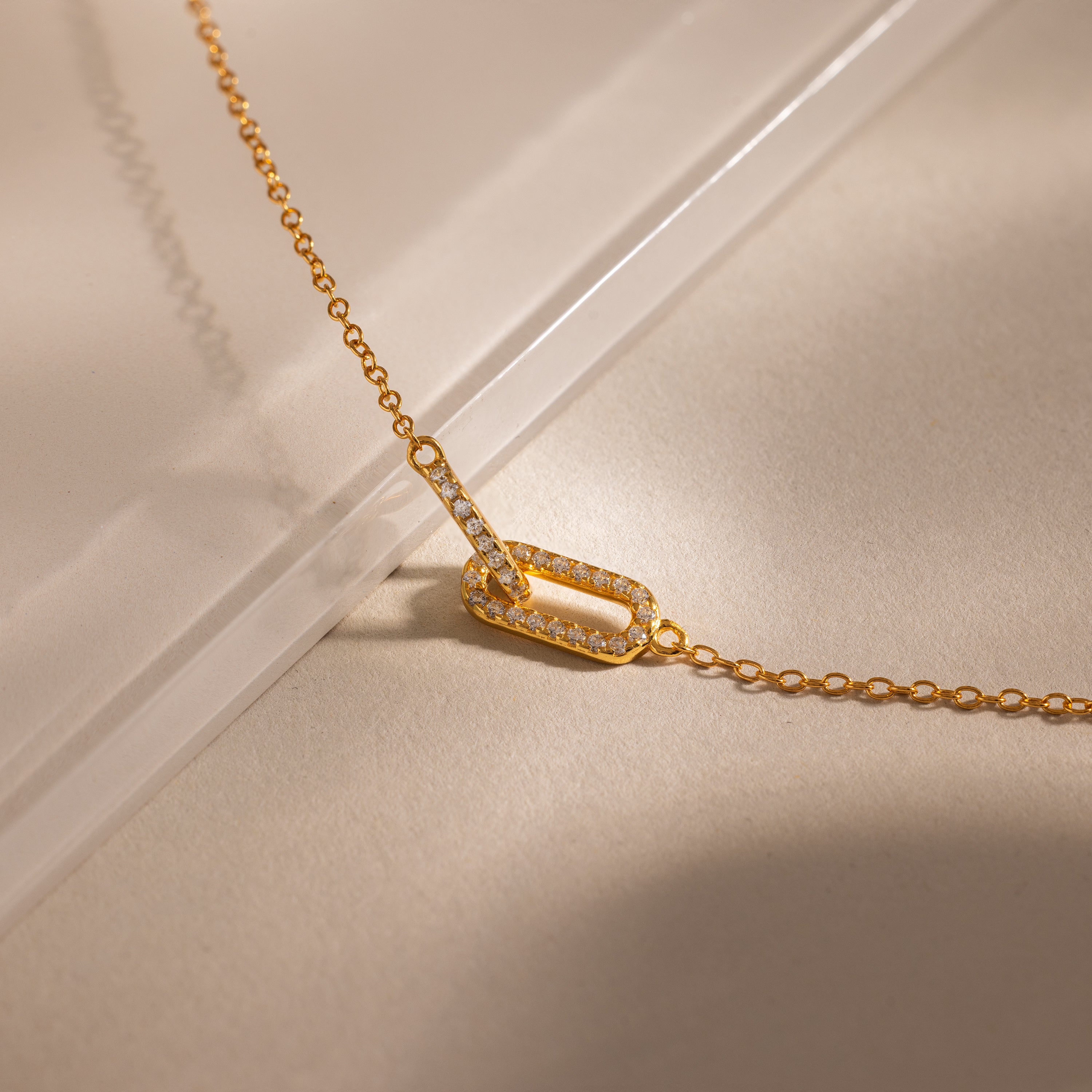 Close-up of a two gold interlocking pave diamond links charms, one circle and one oval link, on a dainty cable chain bracelet.