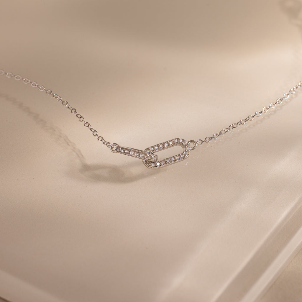 Close-up of a dainty silver chain bracelet featuring two interlocking links charms, one circle and one oval link.