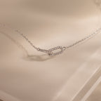 Close-up of a dainty silver chain bracelet featuring two interlocking links charms, one circle and one oval link.