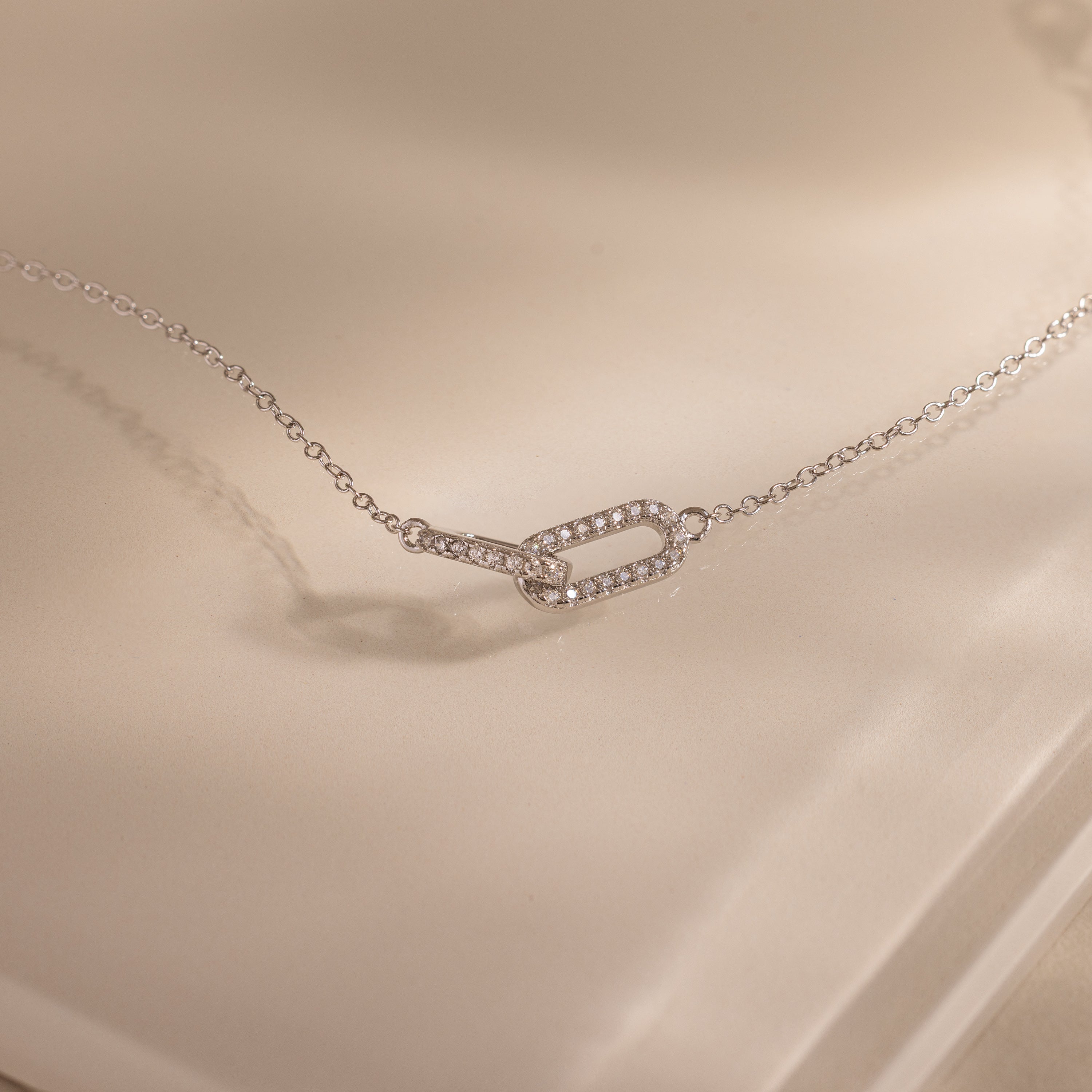 Close-up of a dainty silver chain bracelet featuring two interlocking links charms, one circle and one oval link.