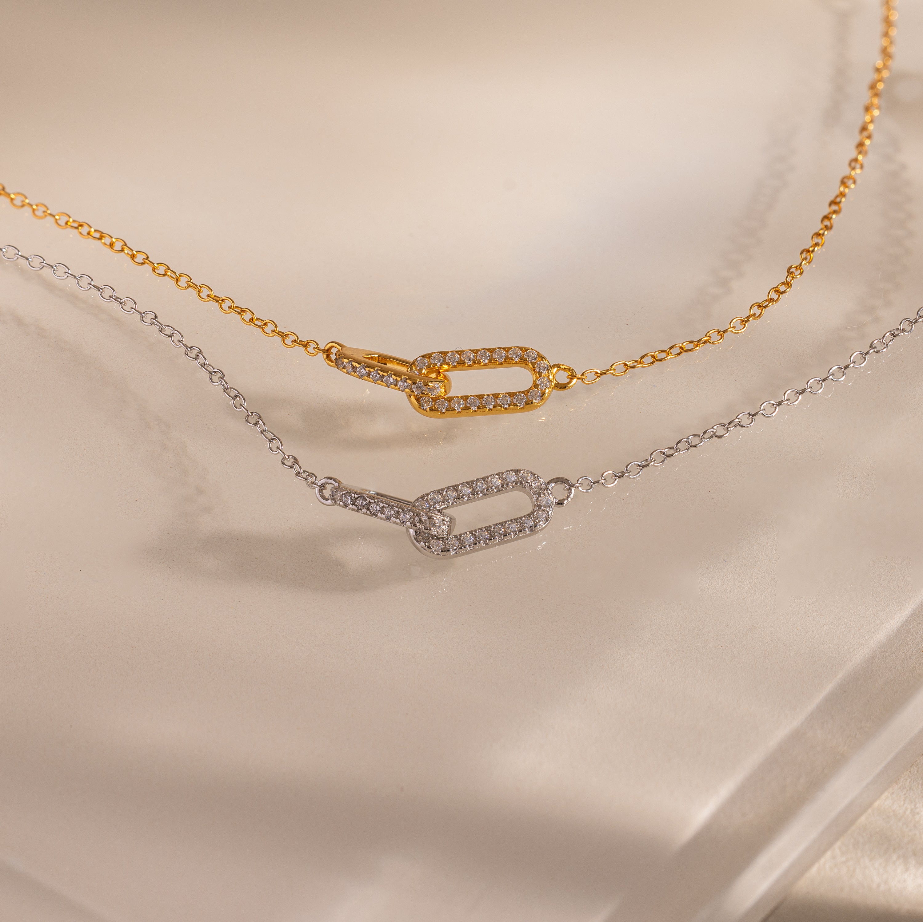 Close-up of a two chain bracelets featuring two interlocking pave links charms, one in gold and one in silver.