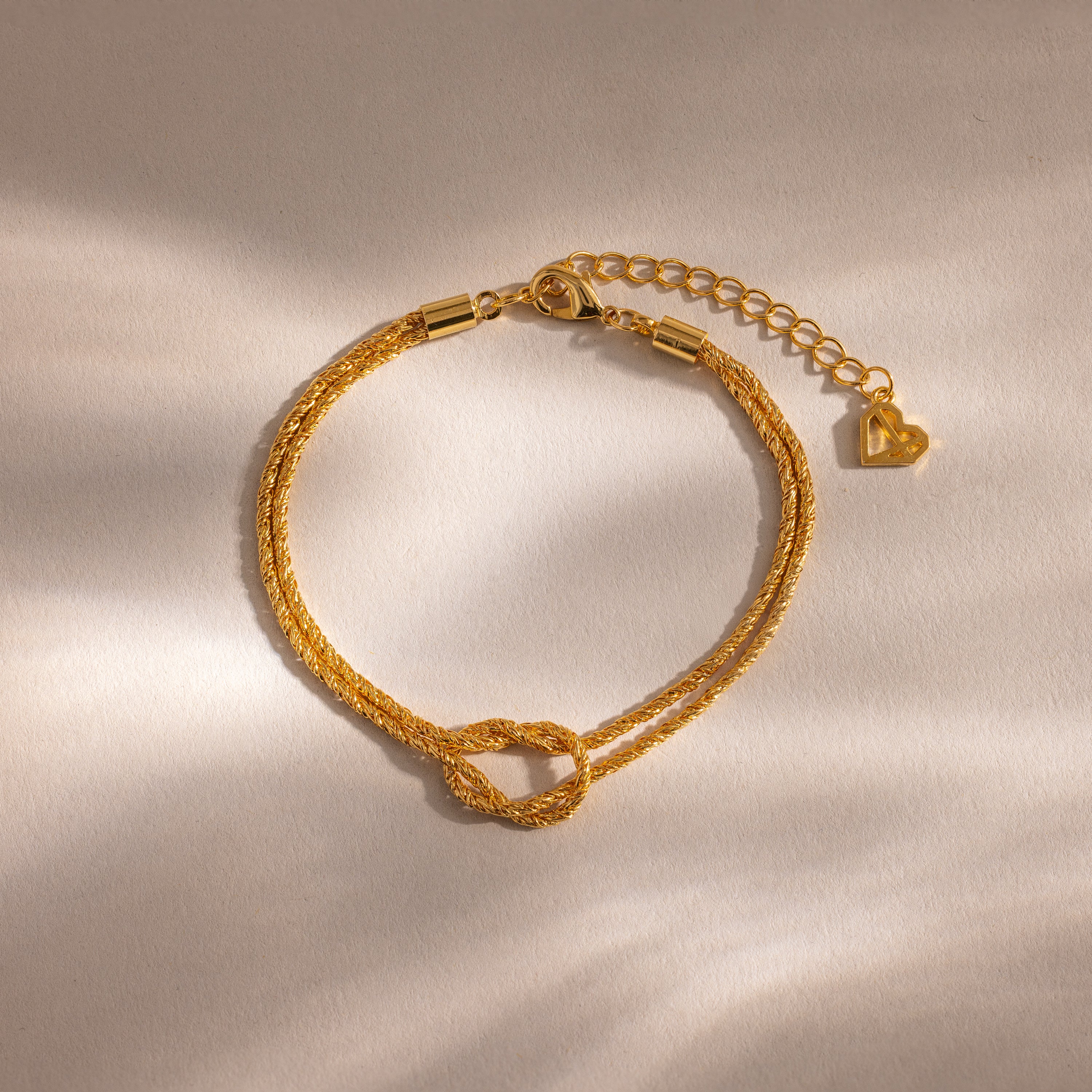 Flat-lay of the Rope Knot Chain Bracelet in gold with a center knot detail and duo chain design, displayed on a neutral background.
