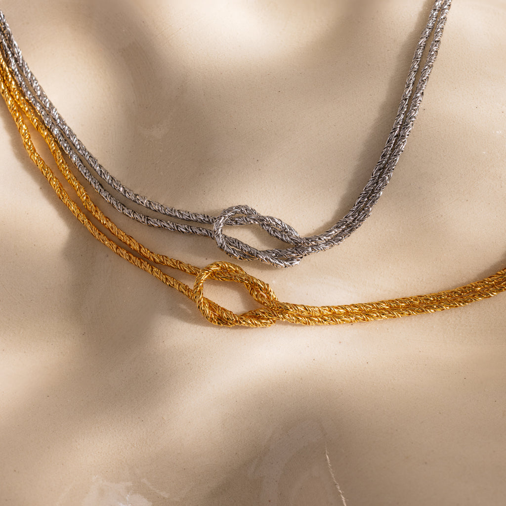 Close-up of two Rope Knot Chain Bracelets in gold and silver, each with a center knot detail, displayed on a neutral background.