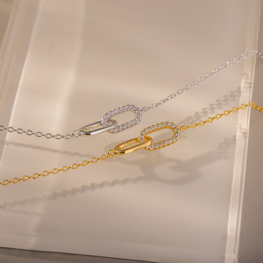 The Pave Linked Pendant Bracelet features interlocking links adorned with sparkling stones, showcasing its gem-encrusted elegance on a beige surface.