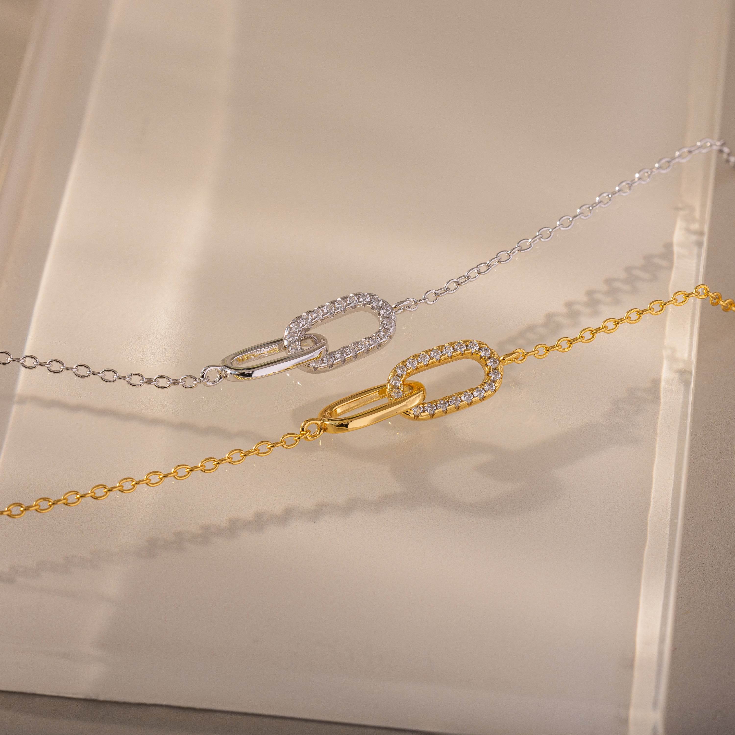 The Pave Linked Pendant Bracelet features interlocking links adorned with sparkling stones, showcasing its gem-encrusted elegance on a beige surface.