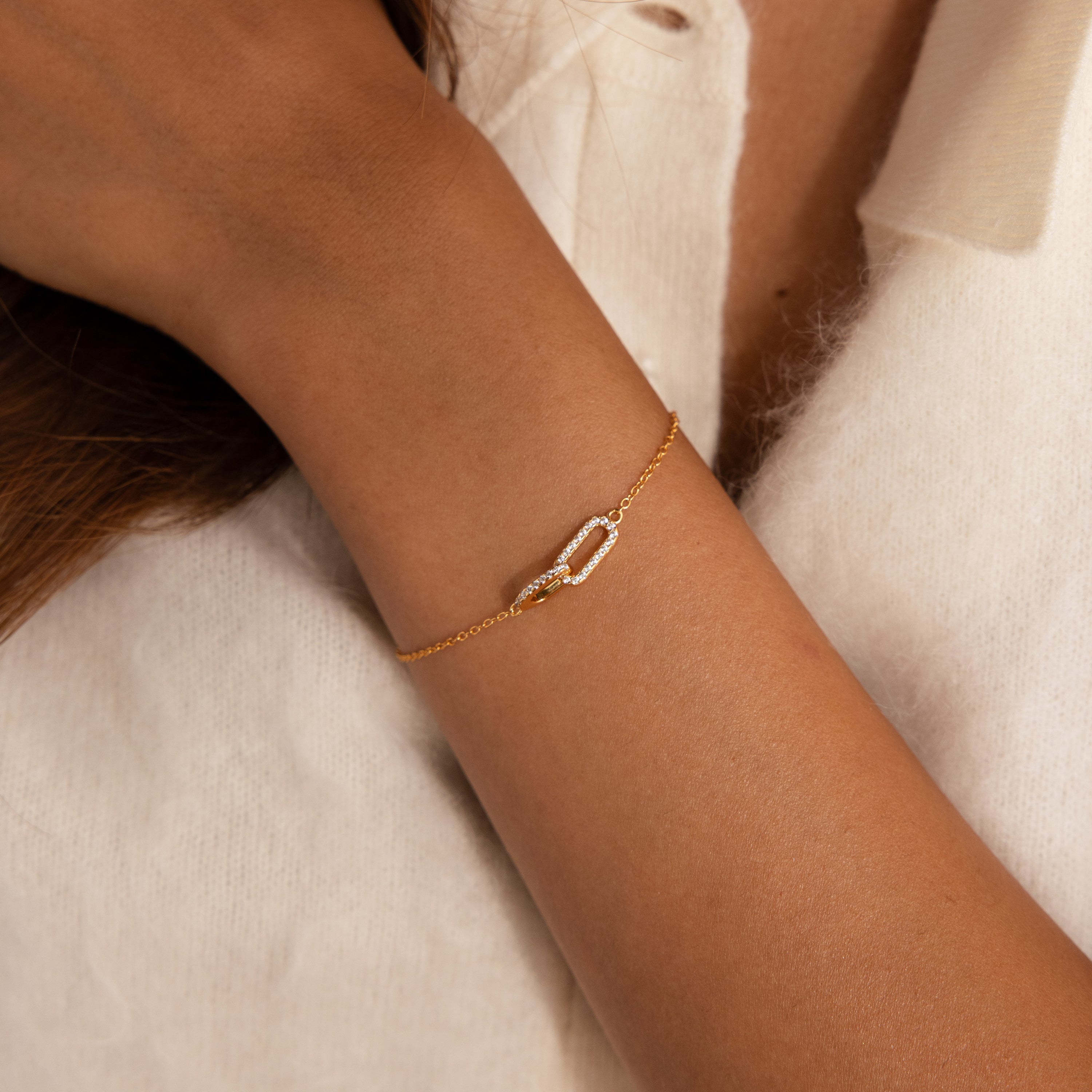 Model wearing a gold chain bracelet featuring two interlocking links charms, one circle and one oval link.