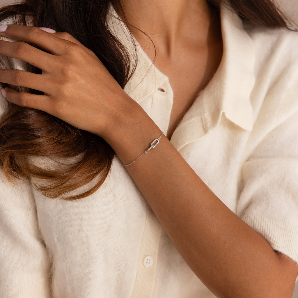 Model wearing a silver chain bracelet featuring two interlocking links charms, one circle and one oval link.