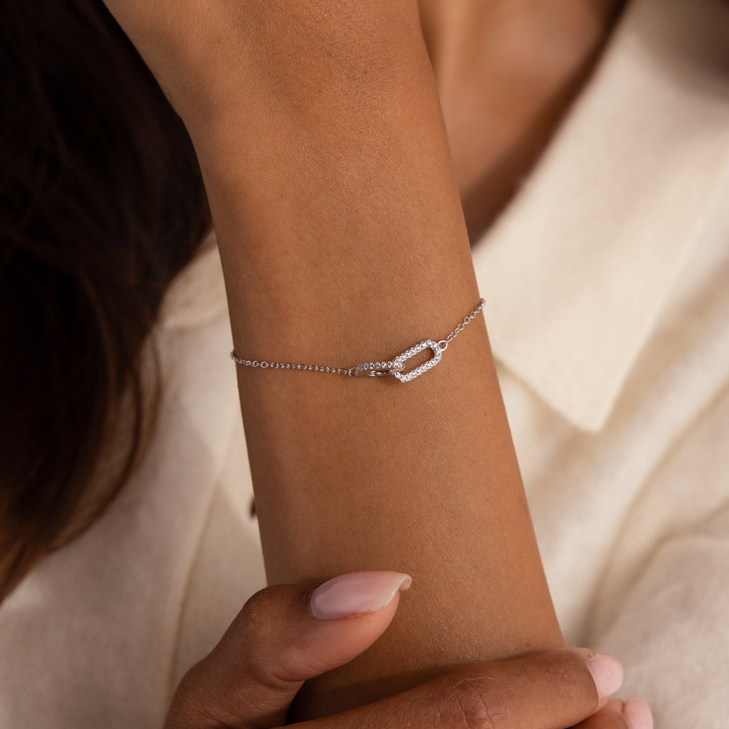Model wearing a silver chain bracelet featuring two interlocking links charms, one circle and one oval link.