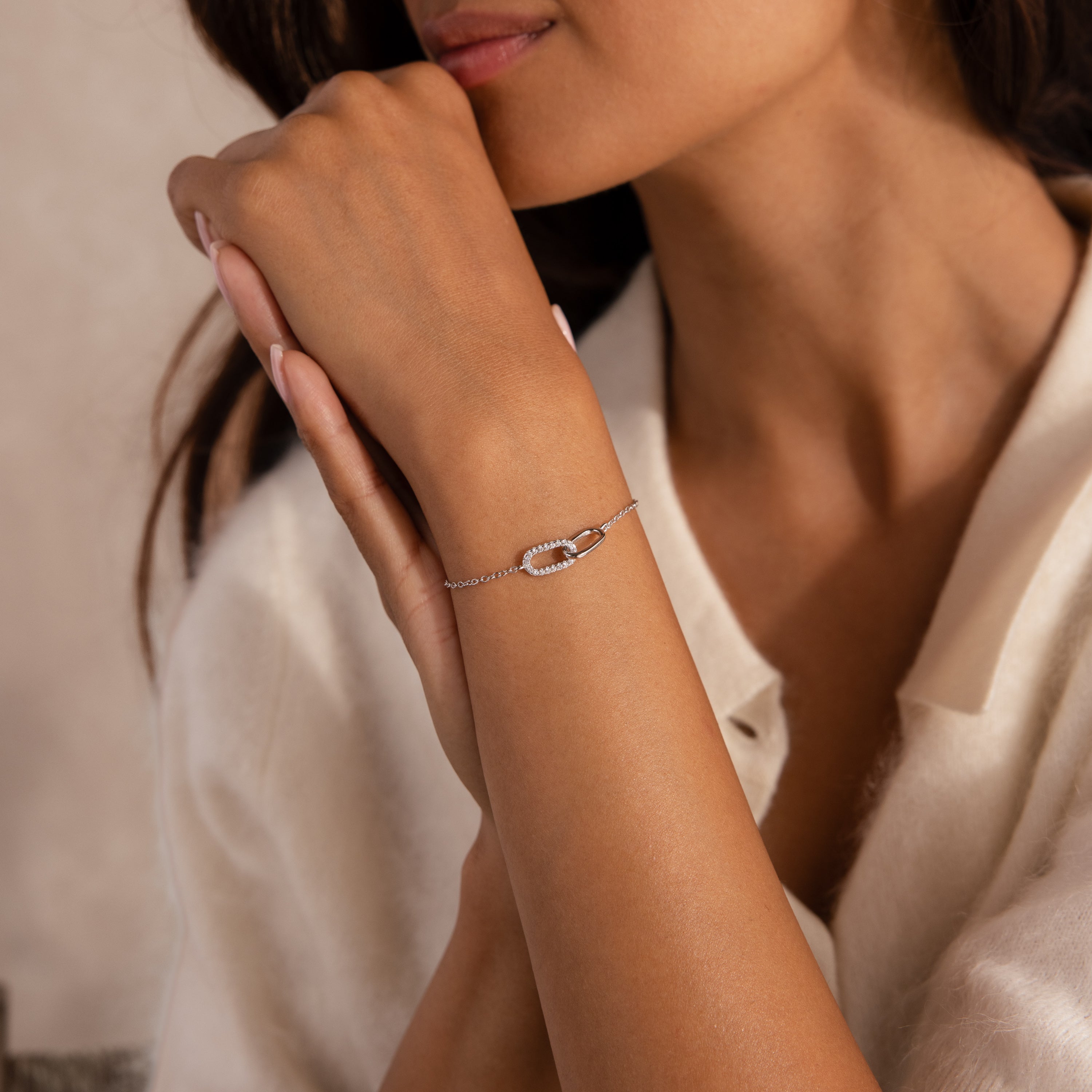 Woman wearing a delicate silver chain bracelet featuring an interlocking link pendant with one pave-set link.