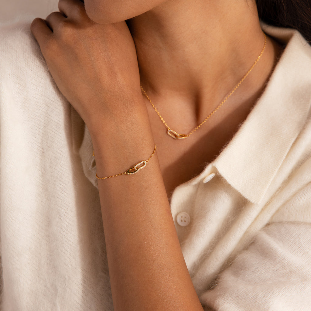 Model wearing a gold chain bracelet featuring two interlocking pave links charms, styled with a matching pave link necklace.