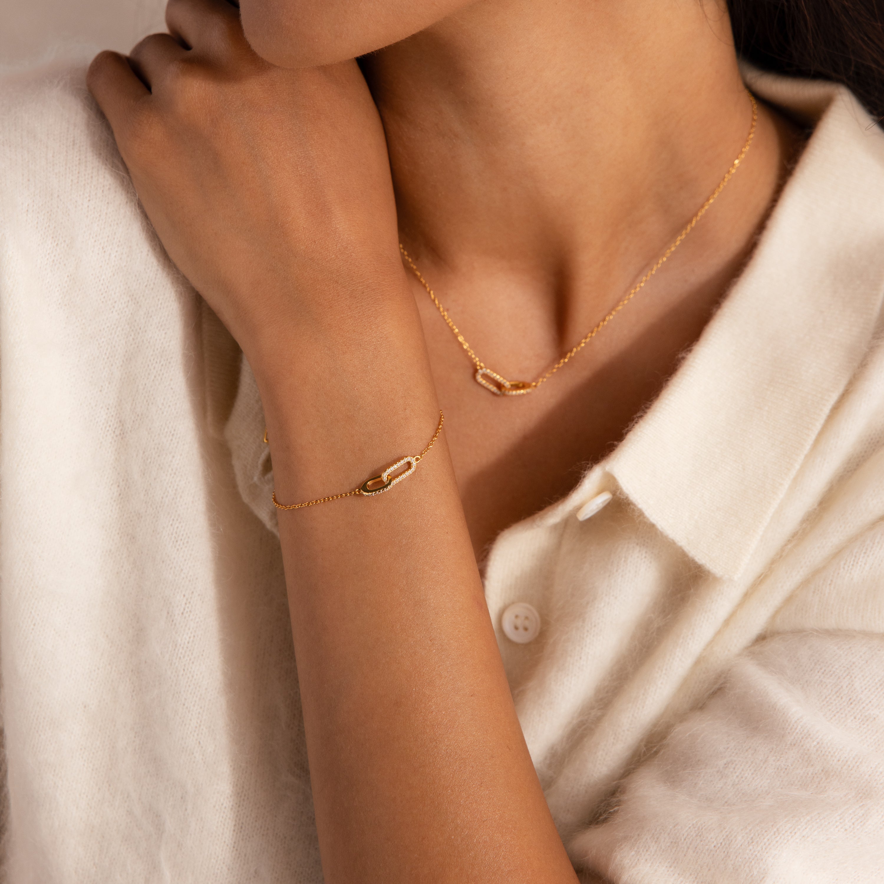 Model wearing a gold chain bracelet featuring two interlocking pave links charms, styled with a matching pave link necklace.