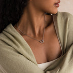 Woman wears the Heart Carabiner Set in Sterling Silver necklace, paired with a light green shawl and cream top, as she gazes to the side.