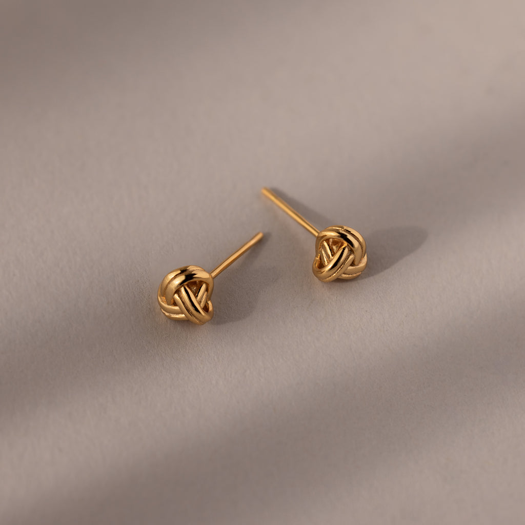 Pair of gold knot earrings on a beige background