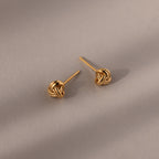 Pair of gold knot earrings on a beige background