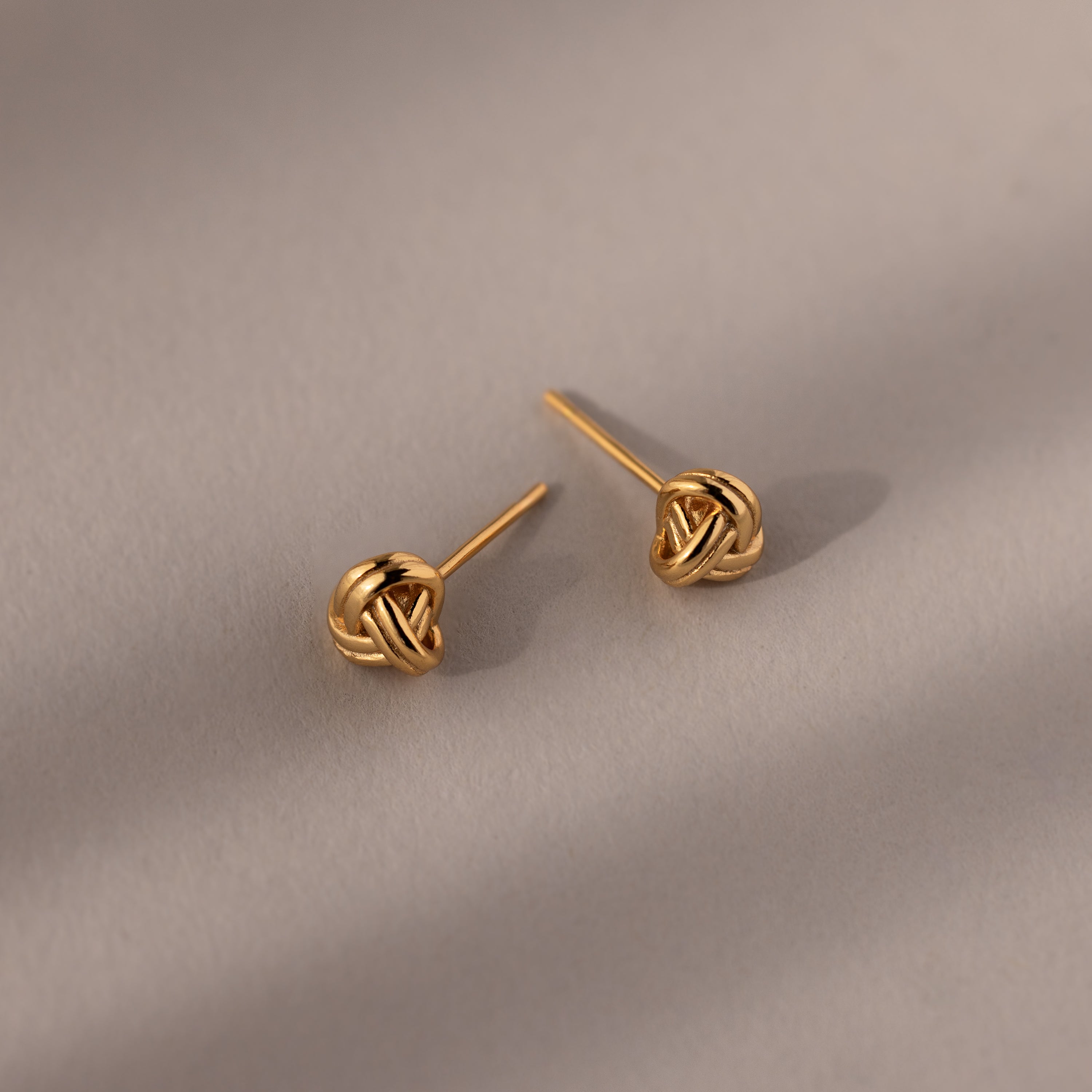 Pair of gold knot earrings on a beige background