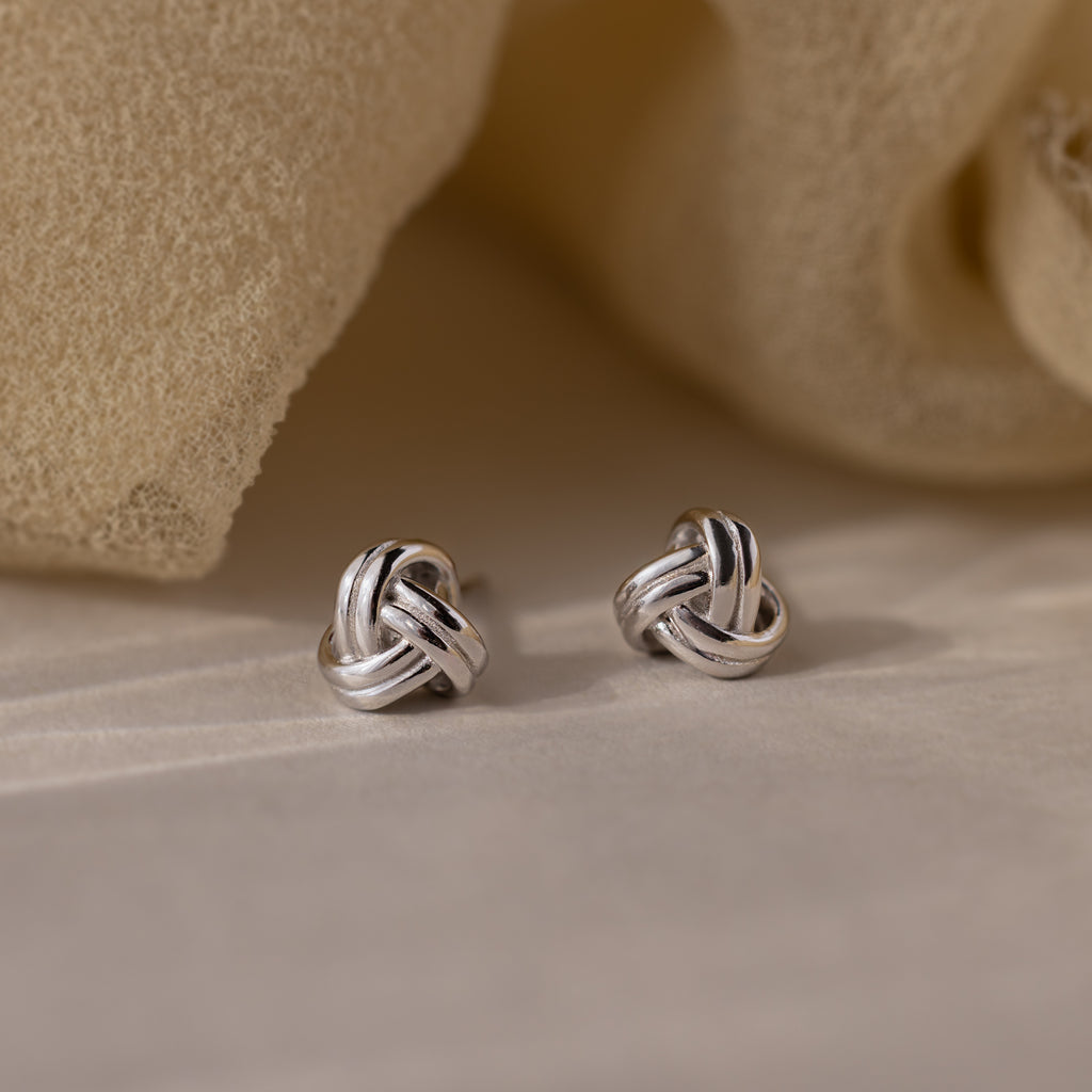 Silver knot earrings on a beige fabric background