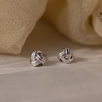 Silver knot earrings on a beige fabric background
