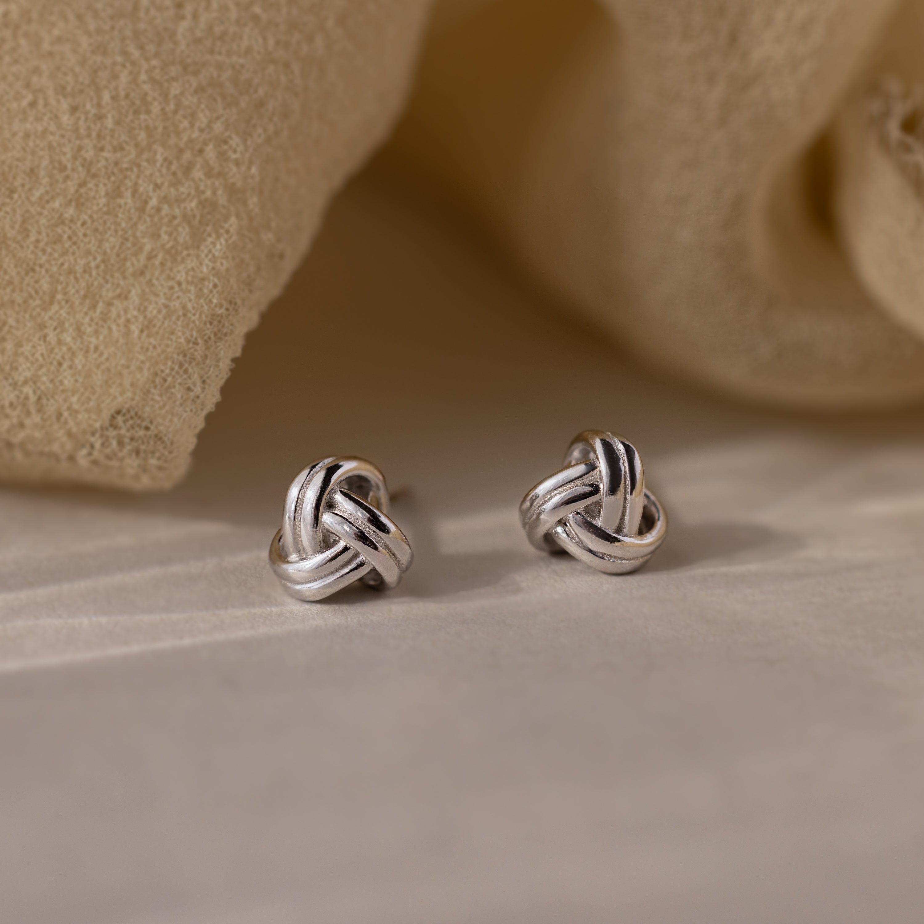 Silver knot earrings on a beige fabric background
