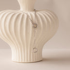 Rolo Lariat Paperclip Clasp Necklace in White Gold with circular links draped over a textured white ceramic vase on a neutral background.
