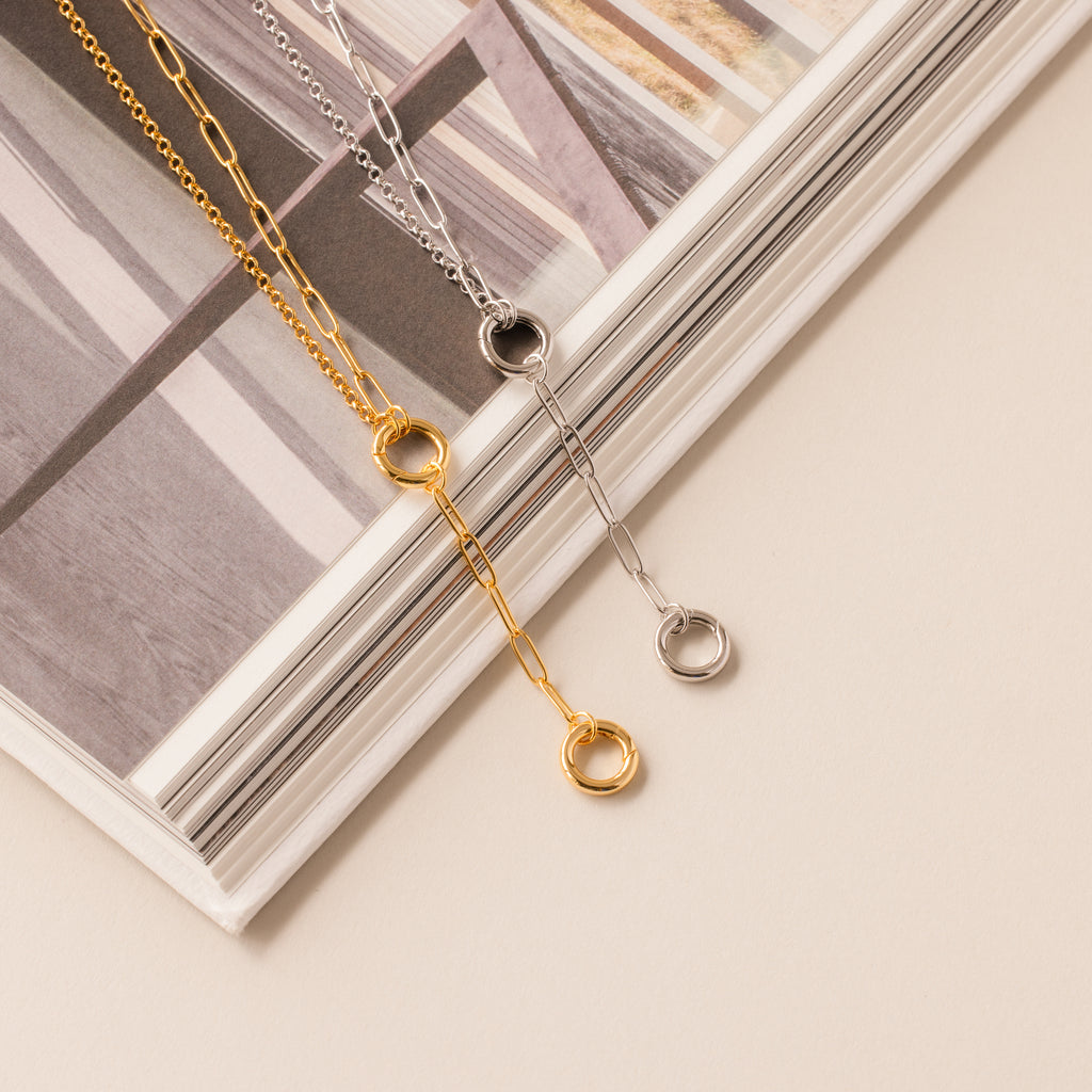 The Rolo Lariat Paperclip Clasp Necklace in White Gold is displayed on an open book with a beige background.
