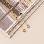The Rolo Lariat Paperclip Clasp Necklace in White Gold is displayed on an open book with a beige background.