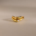 The Zen Gemstone Curve Ring, featuring a small diamond and minimalist gold band, is displayed alongside a light green gemstone-accented ring on a neutral background.