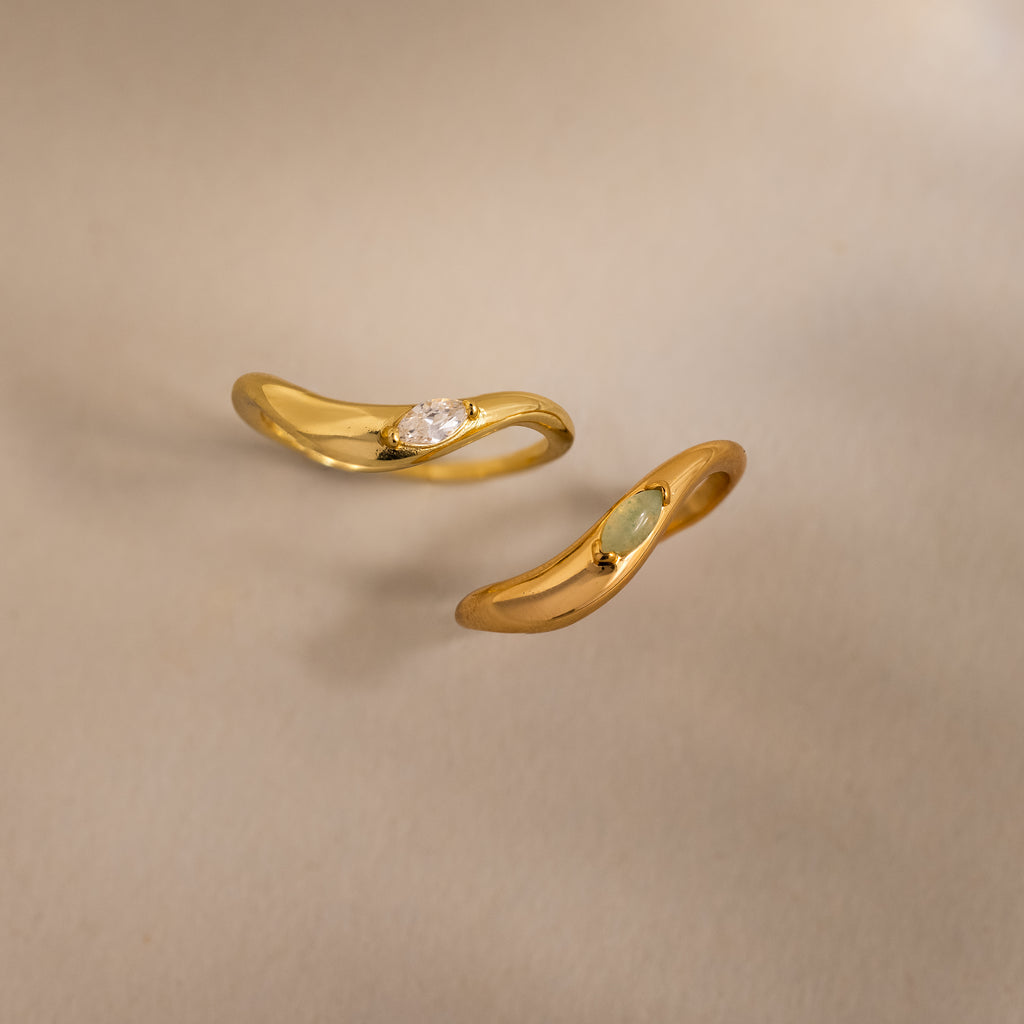 Two gold rings with sculpted bands and small gemstones are displayed on a neutral background, echoing the elegance of the Zen Jade Curve Ring.