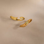 Two gold rings with sculpted bands and small gemstones are displayed on a neutral background, echoing the elegance of the Zen Jade Curve Ring.