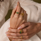 Close-up of manicured hands wearing the Marquise Jade Signet Ring, featuring nature-inspired designs and sparkling green stones.