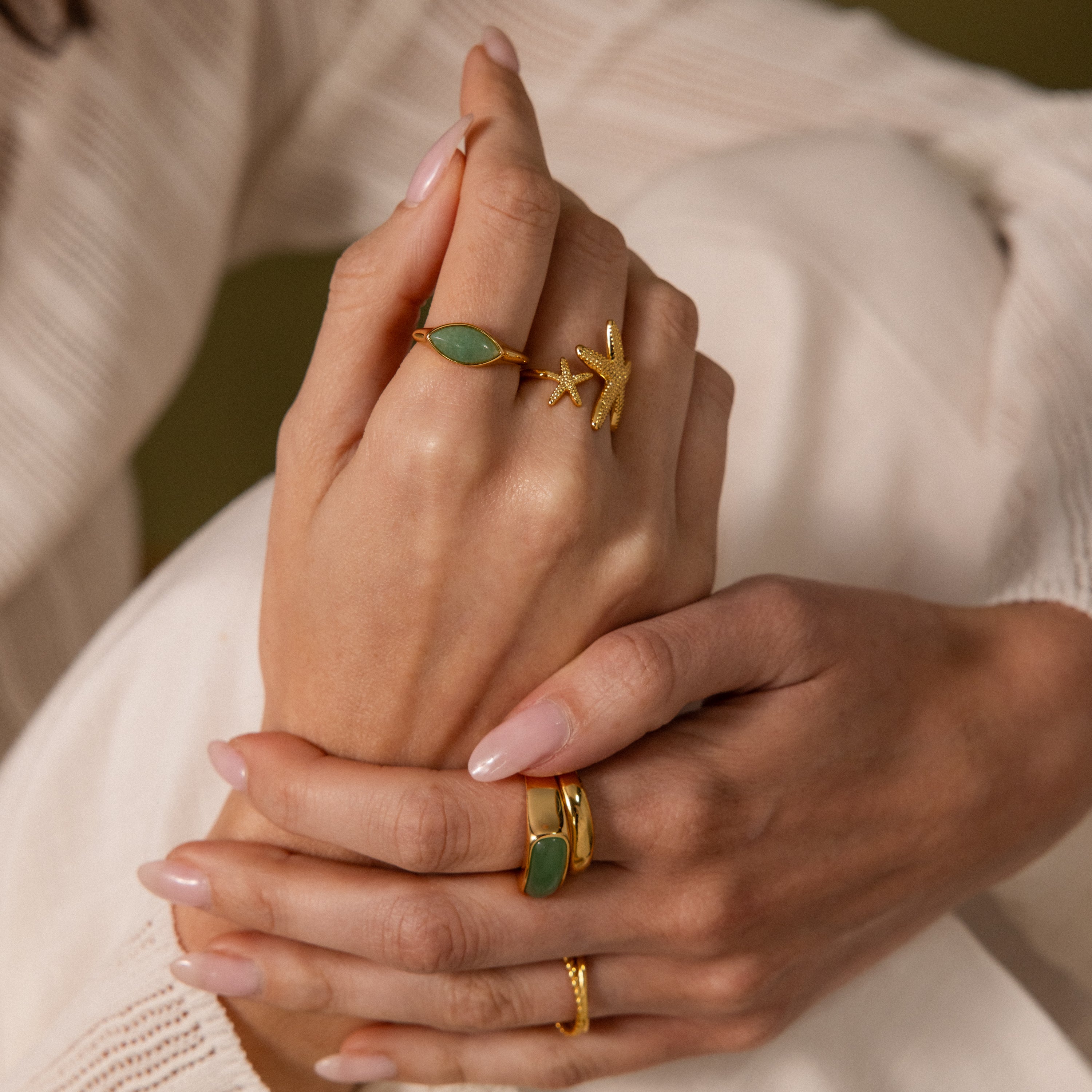 Close-up of manicured hands wearing the Marquise Jade Signet Ring, featuring nature-inspired designs and sparkling green stones.