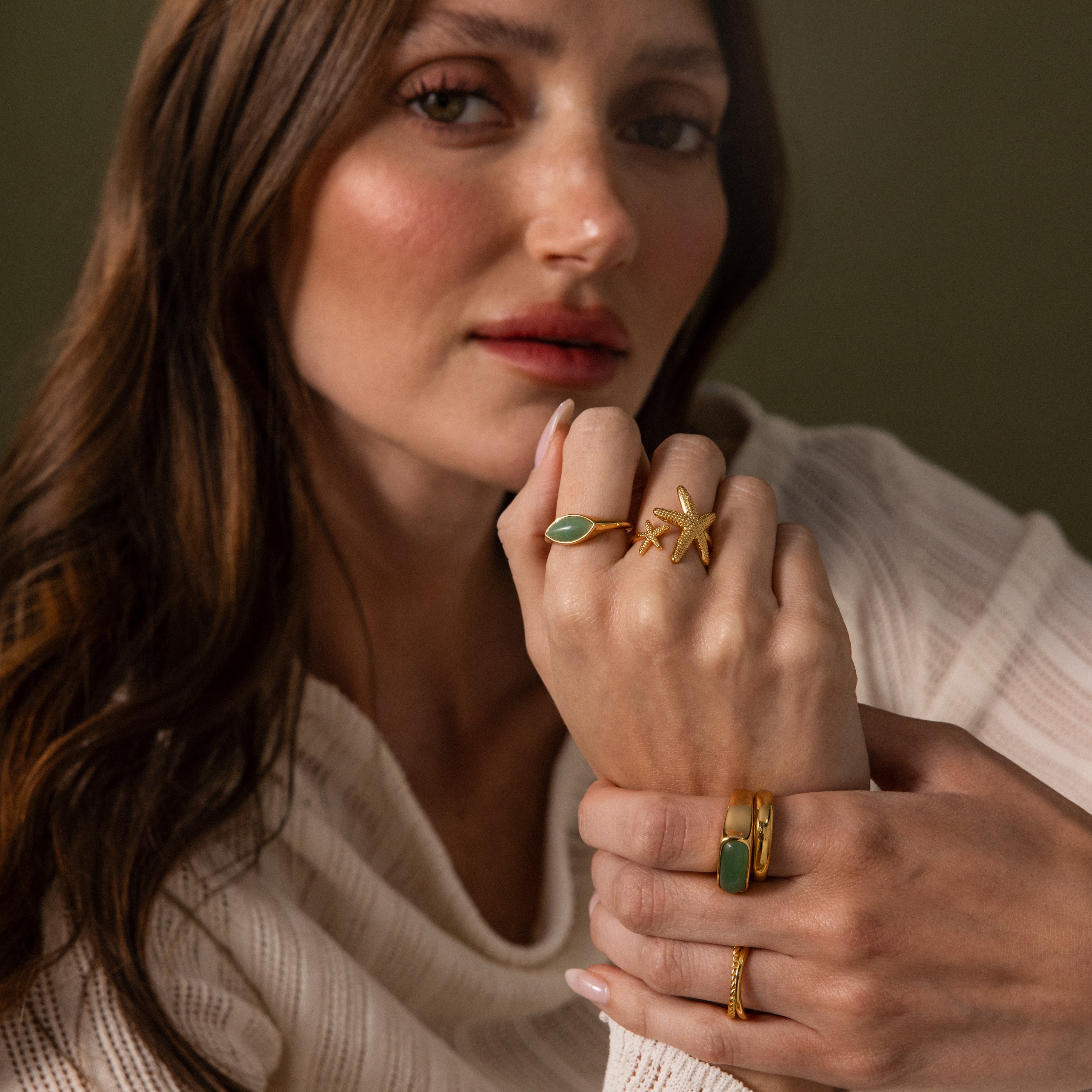 Woman wearing a white top, showcasing the Marquise Jade Signet Ring and a gold bracelet with green stones, gazing towards the camera.
