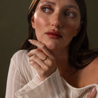 A woman with long brown hair and a white sweater gazes upward, her hand near her chin, elegantly displaying the Zen Jade Curve Ring on her finger.