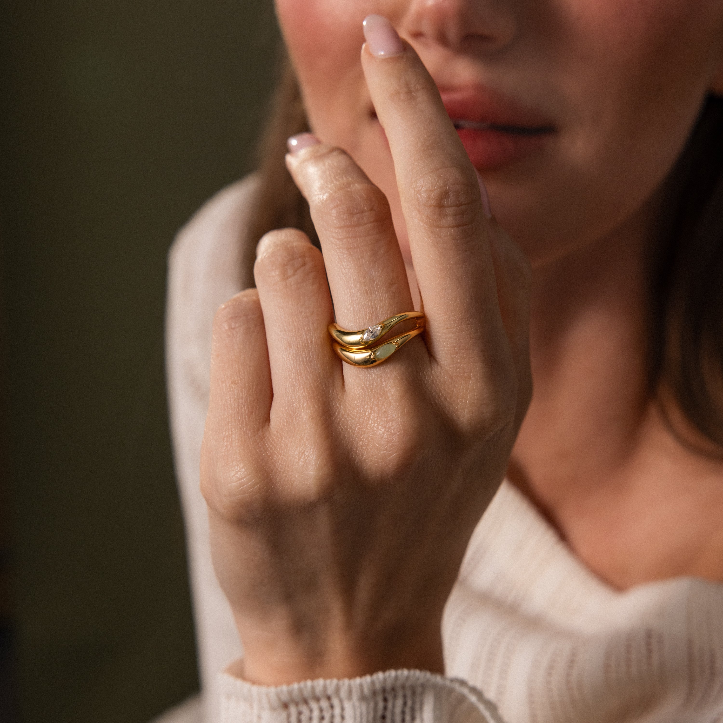 A woman showcases the Zen Gemstone Curve Ring, featuring a sparkling gemstone, as she holds her hand close to her face.