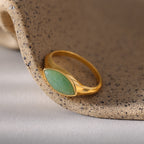 Marquise Jade Signet Ring with an oval green stone, displayed on a textured beige ceramic surface.