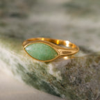 The Marquise Jade Signet Ring, featuring a marquise-shaped green stone, rests on a mottled green and cream surface.