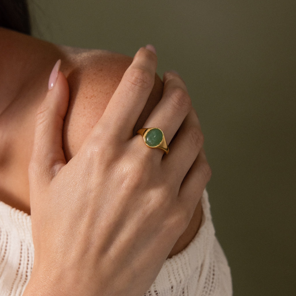 A hand with the Solace Jade Signet Ring—featuring an oval-cut green stone—rests gently on a bare shoulder.
