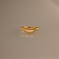 The Zen Jade Curve Ring features a gold sculpted band with a smooth, curved design and a small oval stone set on one side, shown against a neutral background.