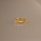 The Zen Jade Curve Ring features a gold sculpted band with a smooth, curved design and a small oval stone set on one side, shown against a neutral background.