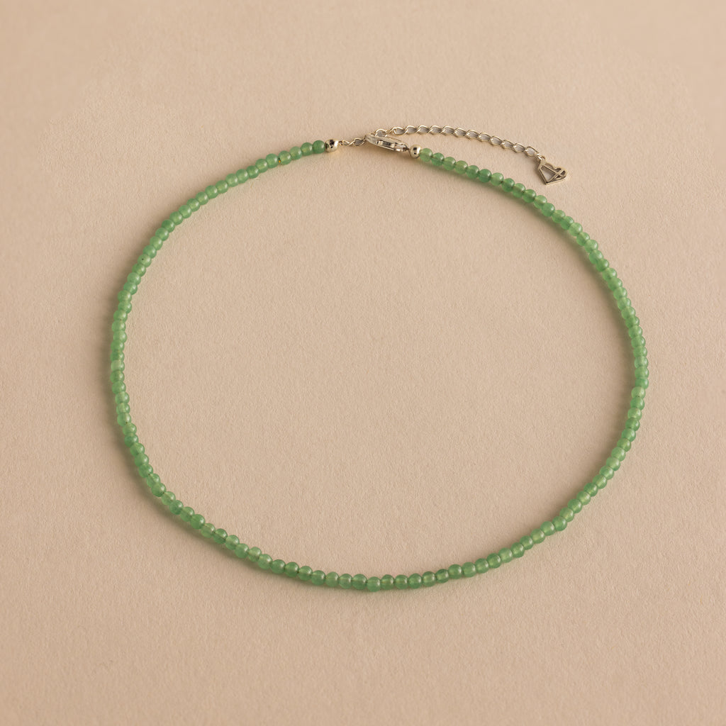 The Tiny Jade Choker Necklace in Silver features delicate green jade beads and a silver clasp with extender, shown on a beige background.