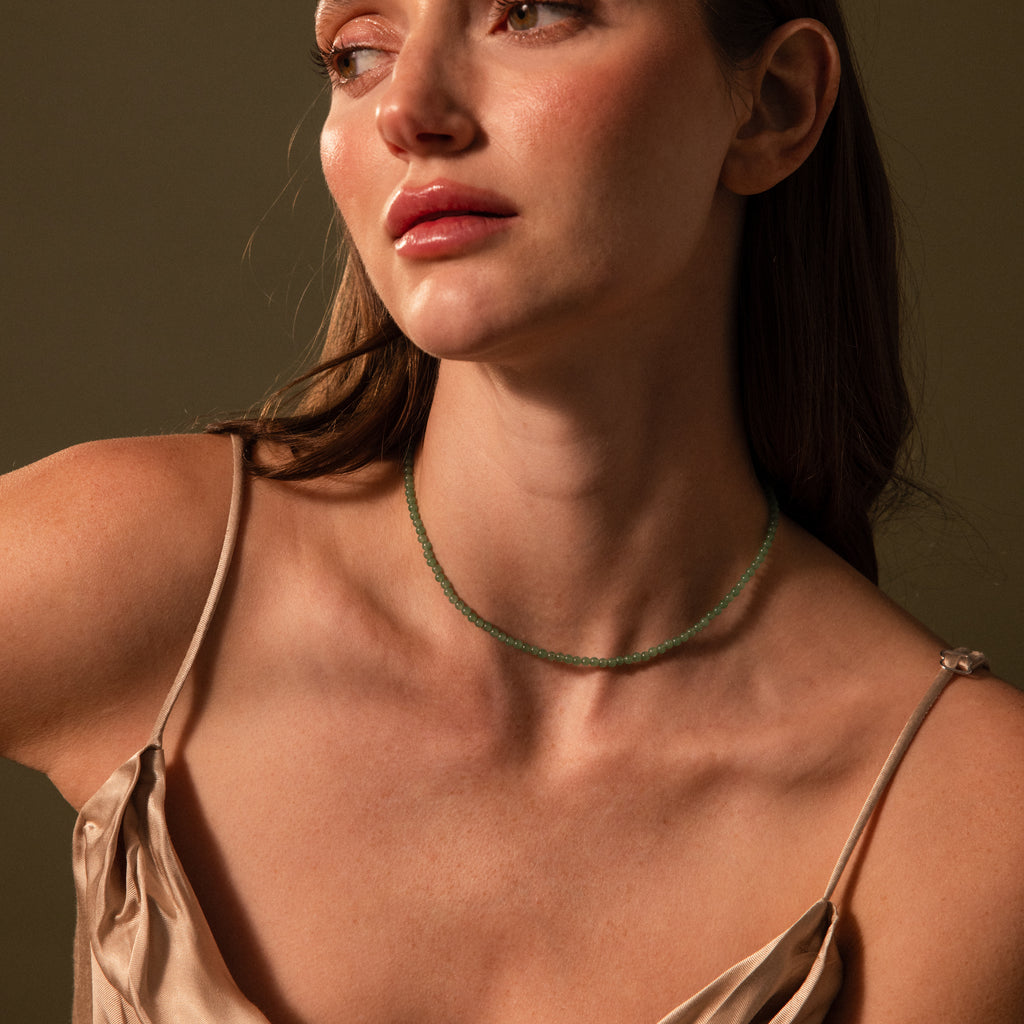 Woman in a satin dress wearing the Tiny Jade Choker Necklace, featuring delicate jade beads, looking to the side against a neutral background.