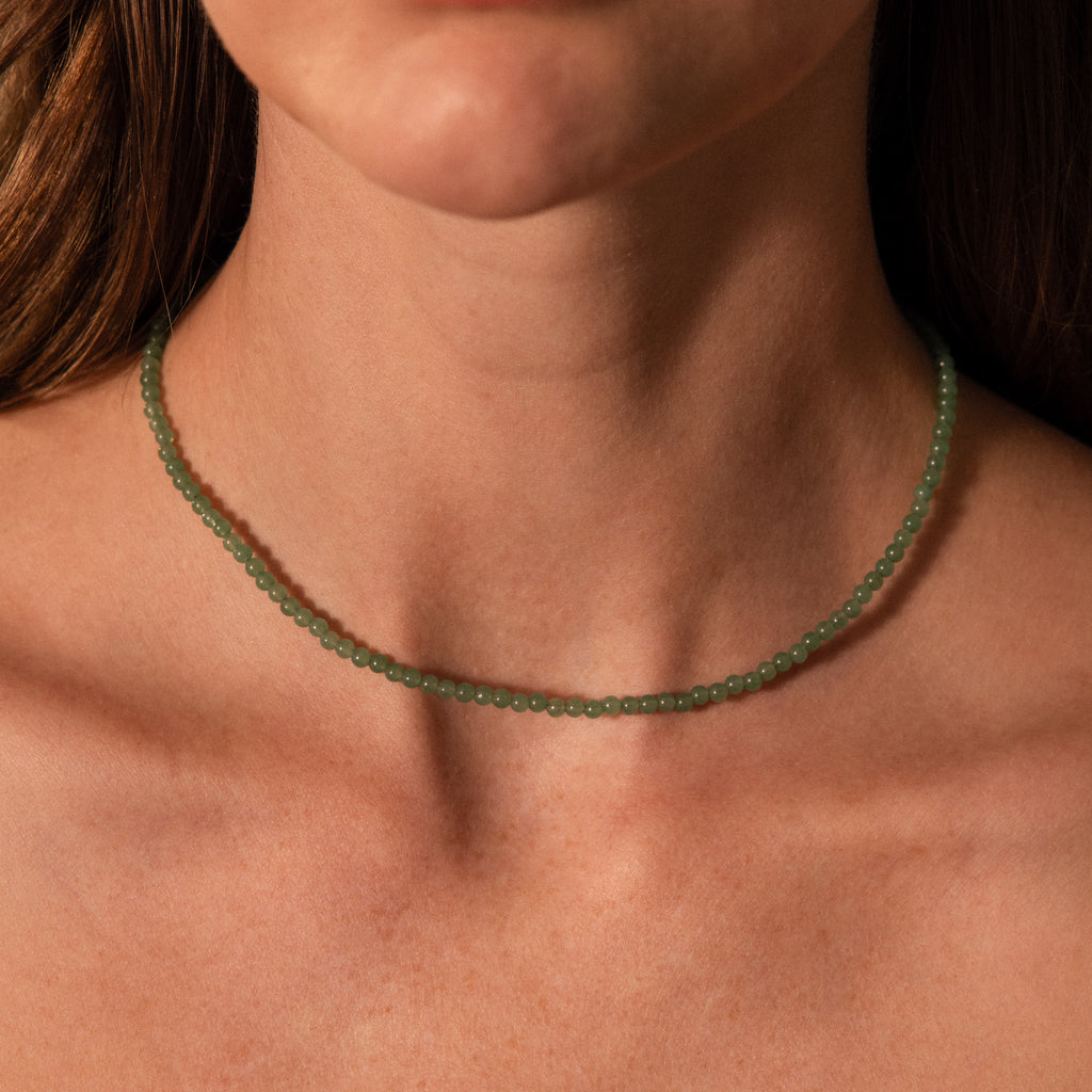 A close-up of a woman's neck adorned with the Tiny Jade Choker Necklace, showcasing delicate green jade beads.