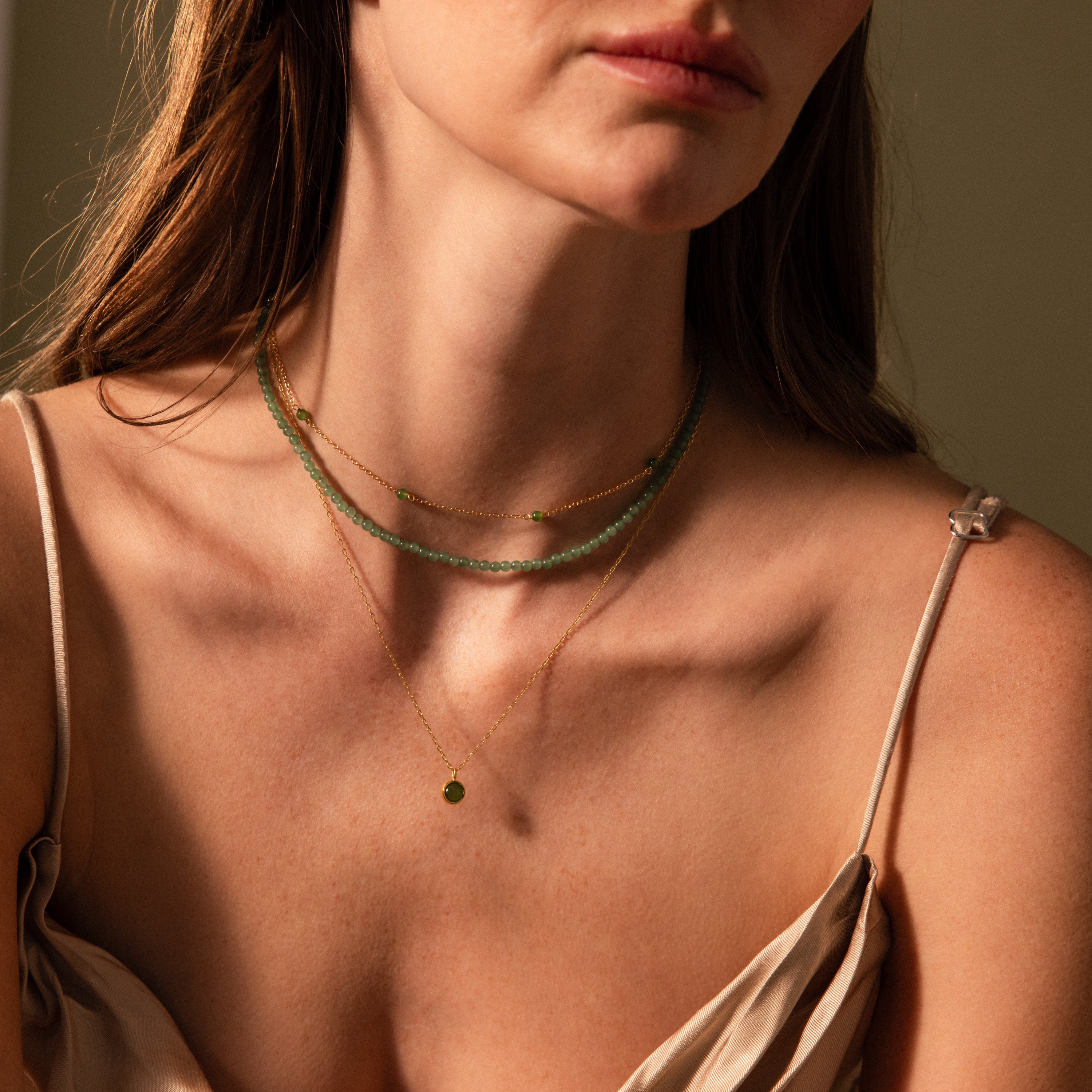 Woman shown from the shoulders up wearing a beige spaghetti strap top and the Tiny Jade Choker Necklace with jade beads and gold accents.