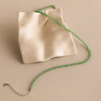 The Tiny Jade Choker Necklace, featuring green beads and a layered design, is displayed on an abstract wavy cream ceramic dish.