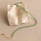 The Tiny Jade Choker Necklace in 18K Gold, with green jade beads and a gold clasp, is displayed on a wavy cream-colored ceramic tray.
