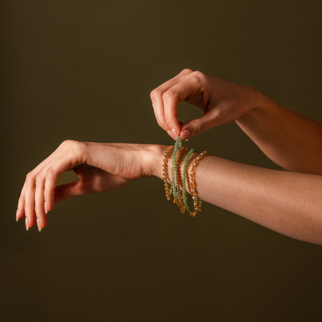 A hand adjusts the Beaded Jade Clasp Bracelet on their wrist, its vibrant green beads gleaming against a plain dark background.